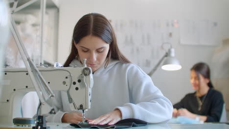 young-womans-hands-seamstress-sitting-and-sews-on-sewing-machine-in-creative-designer-studio.-Two-young-businesswoman-dressmaker-making-new